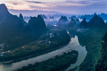 Aerial view of magnificent karst mountain landscape and river winding through the valley at misty twilight in Guilin, China.