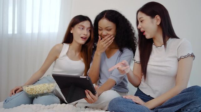 Three young asian women friends share a joyful moment together in bedroom, eagerly looking at their tablet computer and reacting with surprise and delight to the wonderful news they have just found