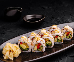 Fresh sushi rolls served with ginger and sauce on a black plate