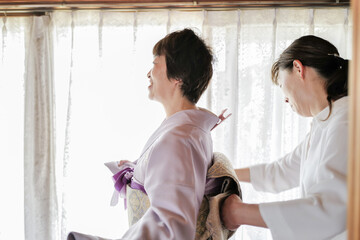 Two women are standing in front of a window, one of them is wearing a kimono. The woman in the...