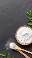 Natural White Flour Poured from Wooden Spoon into Bowl Surrounded by Fresh Green Leaves on Dark Surface 