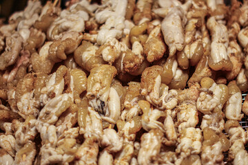 Grilled squid eggs with smoky flavor, golden brown and glossy, stacked on tray. Popular Thai street food often found in night markets and culinary tourism.