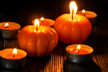 Macro close-up of pumpkin-shaped orange candles and small tealights burning on a dark wooden...