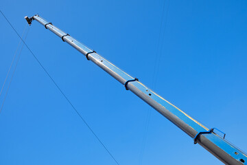 Telescopic crane boom with cables against clear blue sky. Industrial construction equipment detail,...