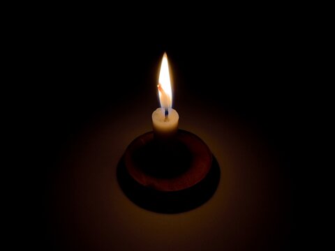 Candle light at night. Burning candle in darkness with focus. White candle burning in the dark, candle flame on wooden board. Light a candle when the lights go out, relaxation and tranquility.