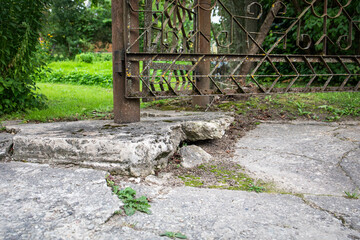 A weathered metal gate attached to a rusty pole standing on broken and crumbling concrete base in a...