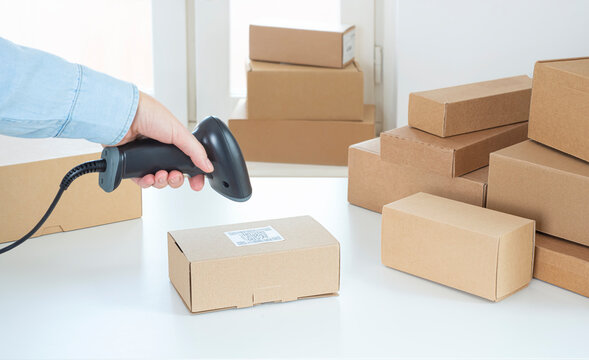 Cropped hand of warehouse worker scanning barcode on cardboard box with handheld reader