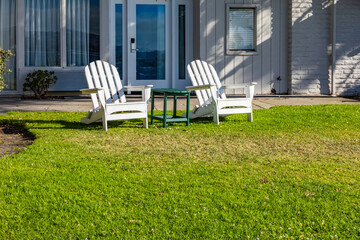 Two white beach chairs on the lawn in front of the house
