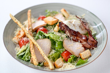 Caesar salad with bacon and grissini on a plate on a white background