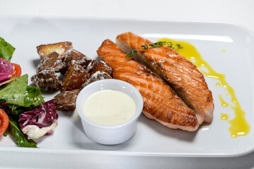 Grilled salmon steak on a plate with salad on a light background