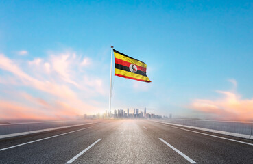 Uganda national flag with mast waving with beautiful skyline. A view from highway. Uganda flag for...