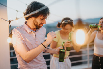 A group of friends having fun with drinks and dancing on a rooftop at sunset.