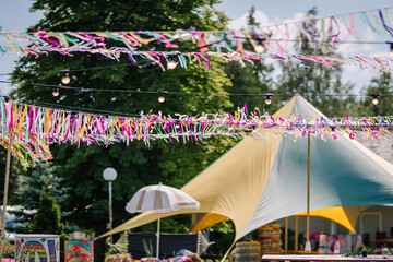 Colorful ribbons and string lights hang over a vibrant outdoor setup with a tent and decor,...