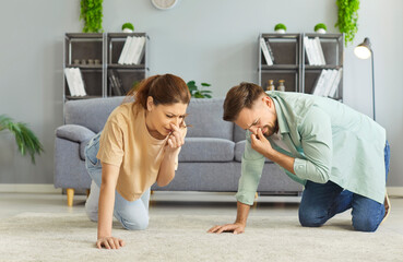 Couple kneeling on floor in living room, covering their noses due to disgusting smell coming from their carpet. Need professional carpet cleaning services to remove dirt, bacteria, unpleasant smells