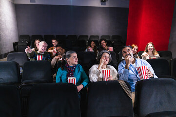 Watching a film while enjoying popcorn, a diverse group of people fills the movie theater with laughter and smiles, sharing a joyful experience