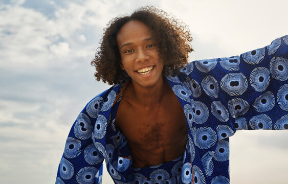Playful man in patterned caftan smiling outdoors on a summer day