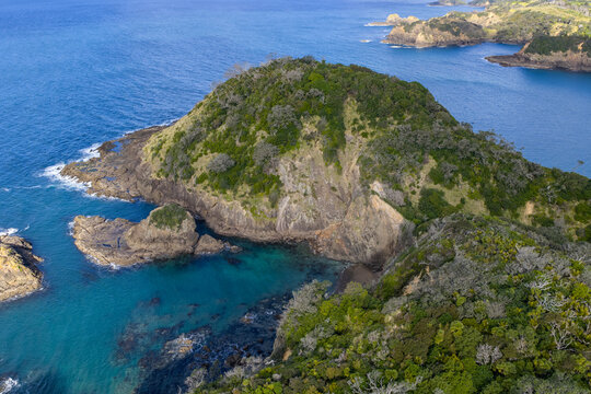 Aerial view of the rugged coastline where rocky cliffs meet the turquoise waters, the lush greenery adding a vibrant contrast, Matapouri, Te Tai-tokerau, New Zealand.