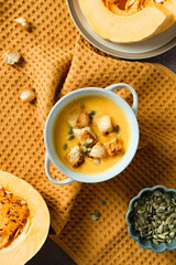 Creamy pumpkin soup with croutons and seeds in bowl, surrounded by fresh pumpkin halves