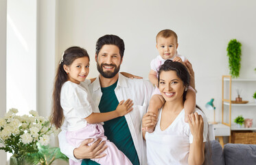 Portrait of smiling young 30s mother and father posing with their little daughter and baby in...