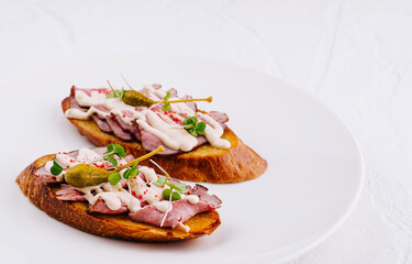 Two delicious bruschetta with meat sauce and capers lying on white plate
