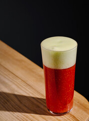 Refreshing red drink in a glass with frothy head on wooden table