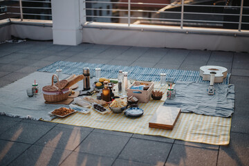 A cozy picnic arranged on a rooftop with assorted food, beverages, and decorative elements alongside a guitar, evoking a sense of leisure, relaxation, and cityscape ambiance.