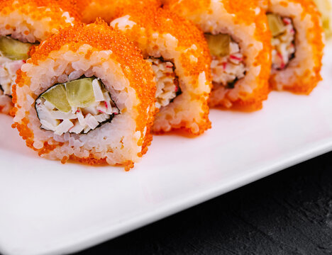 California sushi rolls covered with tobiko red caviar lying on white plate