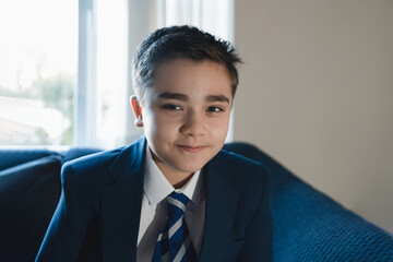 
Portrait of confident schoolboy in uniform sitting indoors with natural light. Concept of Back to...