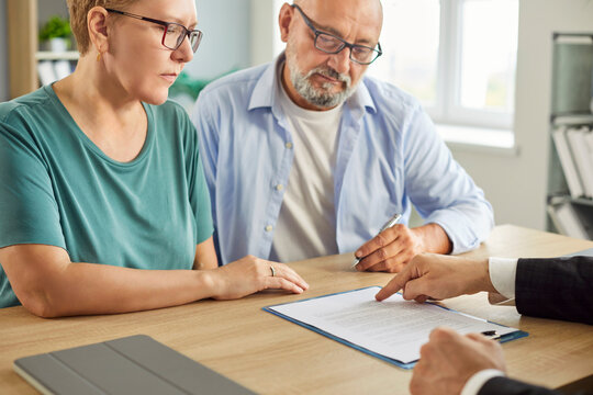 Confident senior couple sitting with financial advisor in office for consultation, signing documents and discussing insurance in retirement. Elderly man and woman sitting with male agent.