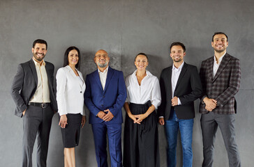 A diverse group of business people stand in a row against studio gray background, expressing unity...