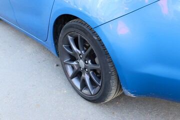 Close-up of the rear wheel and rim of a blue car with scratches on the body — concept of car...