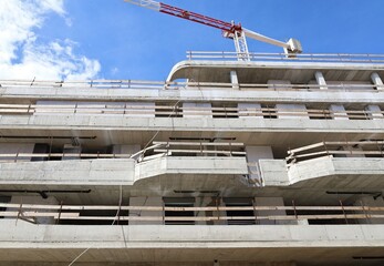 Large building under construction with rough concrete and themal panels exposed. Tower crane and  sky above it. Background for copy space.