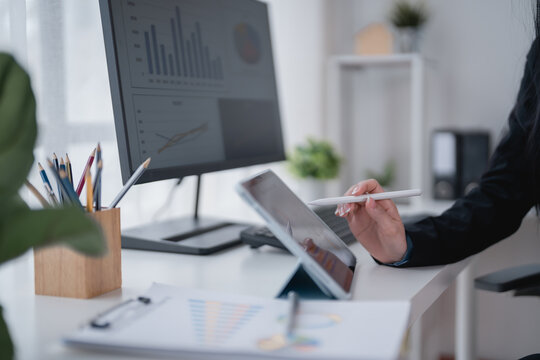 Businesswoman working with stylus pen and digital tablet analyzing financial data displayed on computer screen in modern office, concept of investment and financial analysis