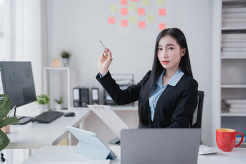 Businesswoman sitting at a desk, working on a laptop and tablet, pointing with a pen while...
