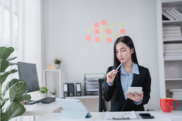 Young businesswoman holding a pen and using calculator while working on digital tablet with...