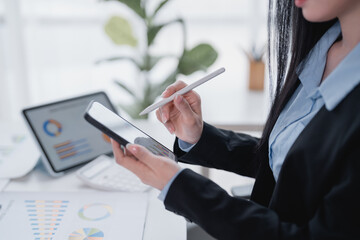 Businesswoman using stylus pen analyzing financial charts and graphs displayed on digital tablet,...