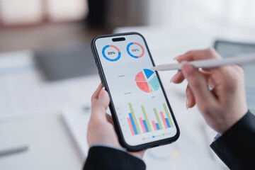 Businesswoman using stylus to analyze financial charts displayed on smartphone screen, enhancing...