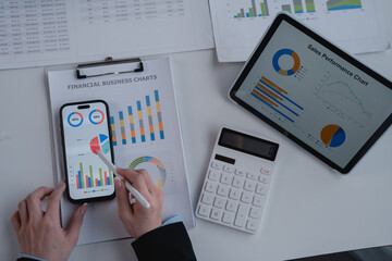 Businesswoman analyzing financial charts on smartphone and tablet while using a calculator to...