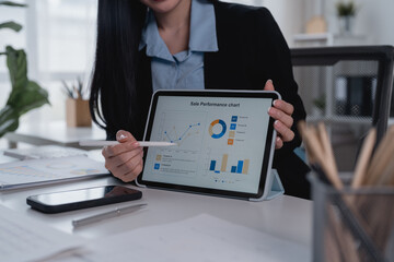 Businesswoman pointing at sales performance chart on digital tablet with stylus, analyzing financial data and business strategy, working at desk in modern office