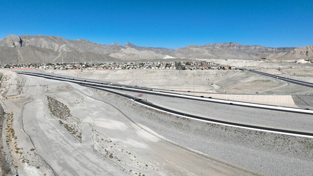 Aerial view of a stark, sun-drenched highway cutting through the arid landscape near rugged mountains, a testament to human engineering against nature's grandeur, Las Vegas, Nevada, United States.