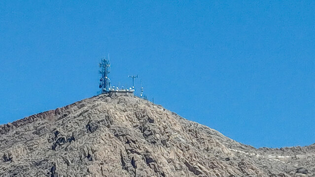 Aerial view of a rugged, rocky mountain peak crowned with a telecommunications tower against a brilliant blue sky, Las Vegas, Nevada, United States.