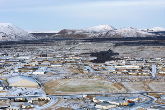 Fototapeta Aerial view of a town nestled beneath snow-dusted mountains and dark lava fields, a stark contrast of white and black, Grindavik, GrindavÃ­kurbÃ¦r, Iceland.