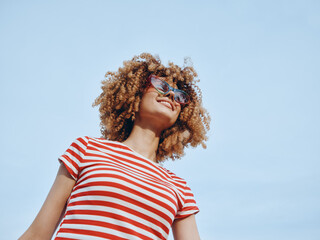 A stylish portrait of a smiling person with curly hair wearing a red and white striped tee and...