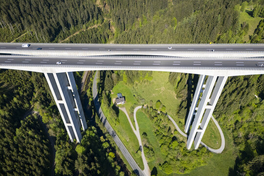 Aerial view of a modern bridge soaring through the verdant landscape, its stark white pillars contrasting with the lush green forest, Wolfsberg, Carinthia, Austria.