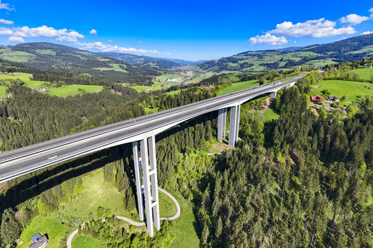 Aerial view of a towering bridge piercing through lush green valleys and forests under a bright sky, Lavanttal, Wolfsberg, Carinthia, Austria.