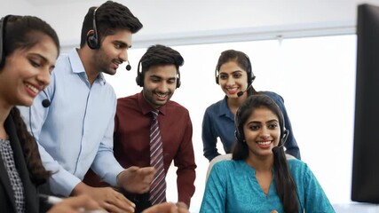 Group of diverse call center workers looking at computer and pointing. Customer service team in office, people with headset, teamwork and technology concept. - Powered by Adobe