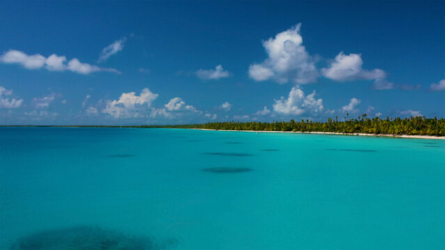 Aerial view of turquoise waters meet the lush green coastline under a vibrant blue sky dotted with fluffy clouds, Bora Bora, French Polynesia.