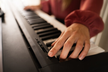 Fototapeta premium Close-up of Caucasian woman's hand turning on an electric piano before starting musician lesson indoors with cozy warm light, selective focus