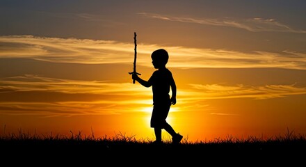 Silhouette of a boy holding a stick against a vibrant sunset
