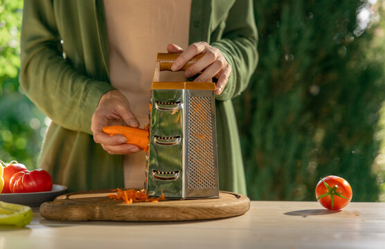Woman grating carrot for salad outdoors in a garden kitchen
